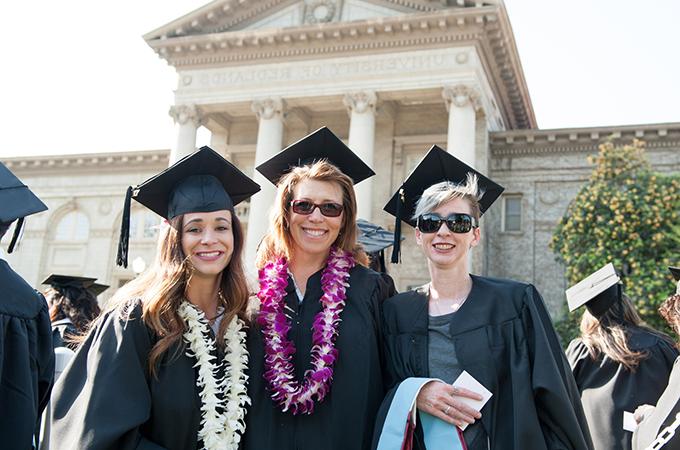Three female students from the School of Education gather in front of the Administration Building after commencement.