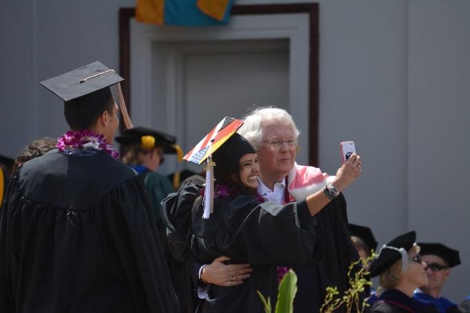 Professor Jack Osborn congratulates a student on the stage during a Commencement ceremony.