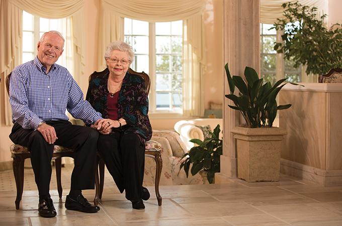 The Hunsakers sit in the foyer of a grand room, holding hands and smiling.