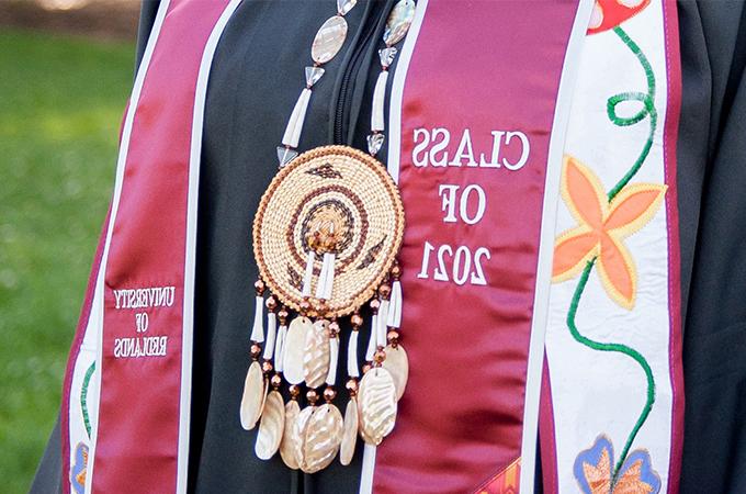 A student pairs a traditional Native American necklace with their Class of 2021 Commencement sash.
